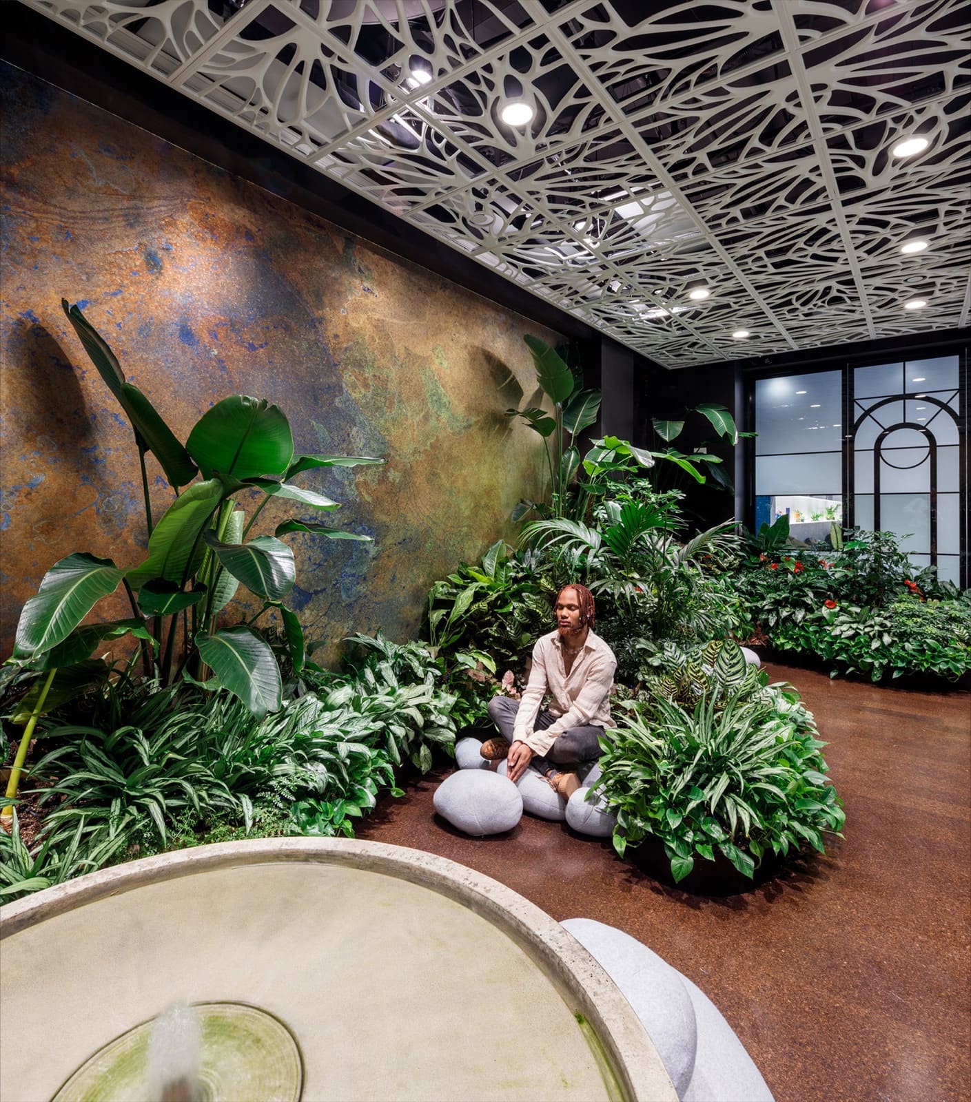 A man meditating in a lush plant-filled wellness space designed by Greenery NYC