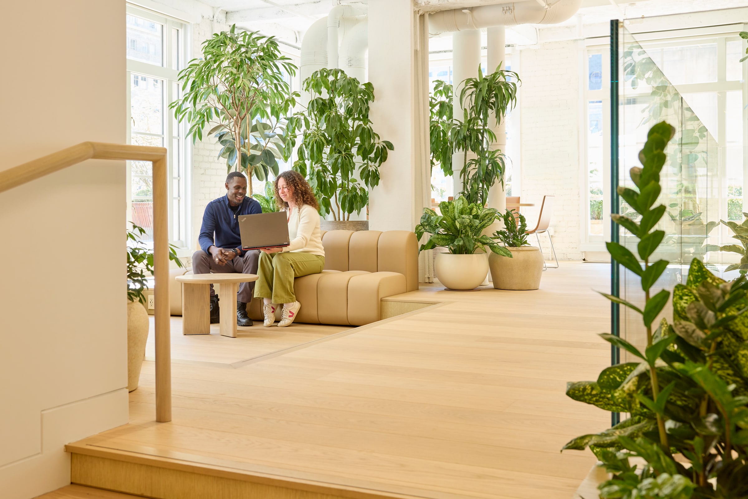 Two colleagues working together on a sofa surrounded by trees and daylight at Tishman Speyer's New York headquarters
