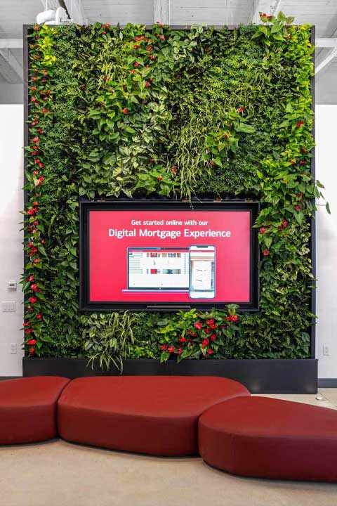 Vibrant green wall with plants and a large screen in the room. Red, curved seats sit in front of the green wall which holds anthuriums.