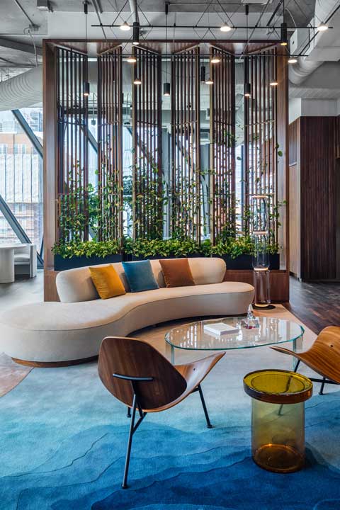 Modern office lounge area with a curved sofa, climbing vines, and designer furniture.